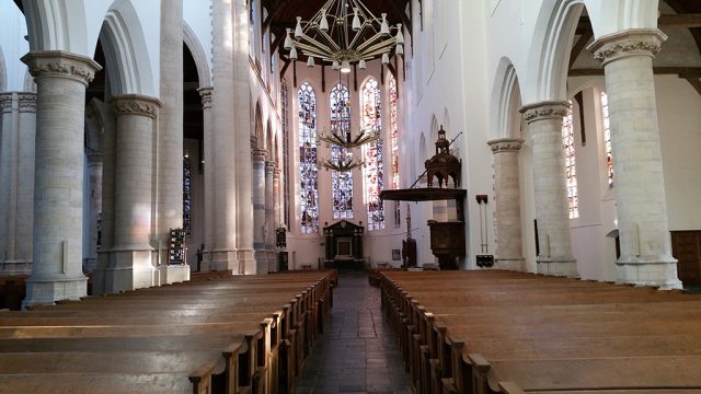 An old church interior with benches, pillars and stained glass windows