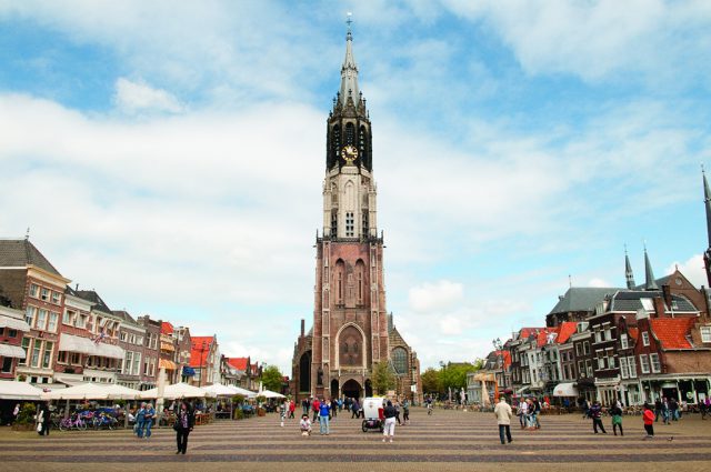 A churchtower on a square with people in between houses
