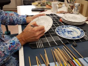 A person making a drawing on a plate with pencils and paint