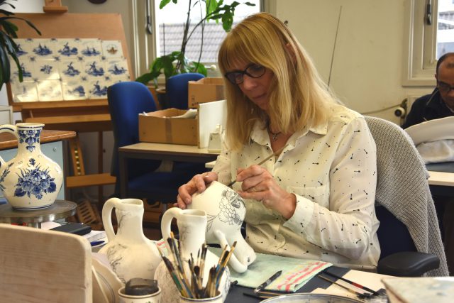 A woman making a drawing on a pottery vase with a pencil