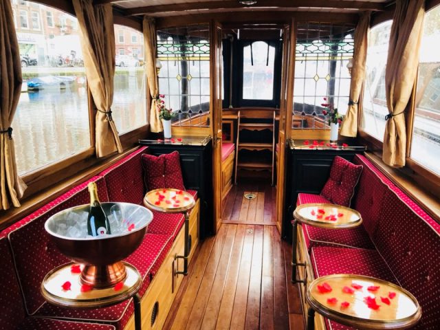 The interior of a salonboat with benches, tables and a bottle of champaign