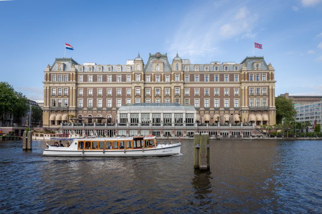 A saloonboat on a river in front of a big building with many windows