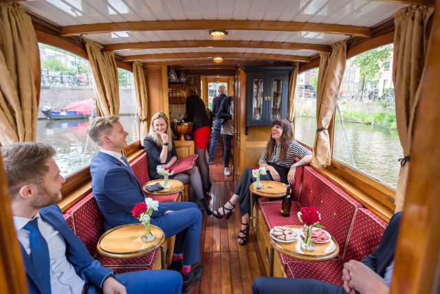people sitting and standing with drinks and snacks in a saloonboat
