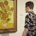 A men looking at a Van Gogh painting of sunflowers in a vase.
