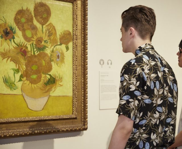 A men looking at a Van Gogh painting of sunflowers in a vase.