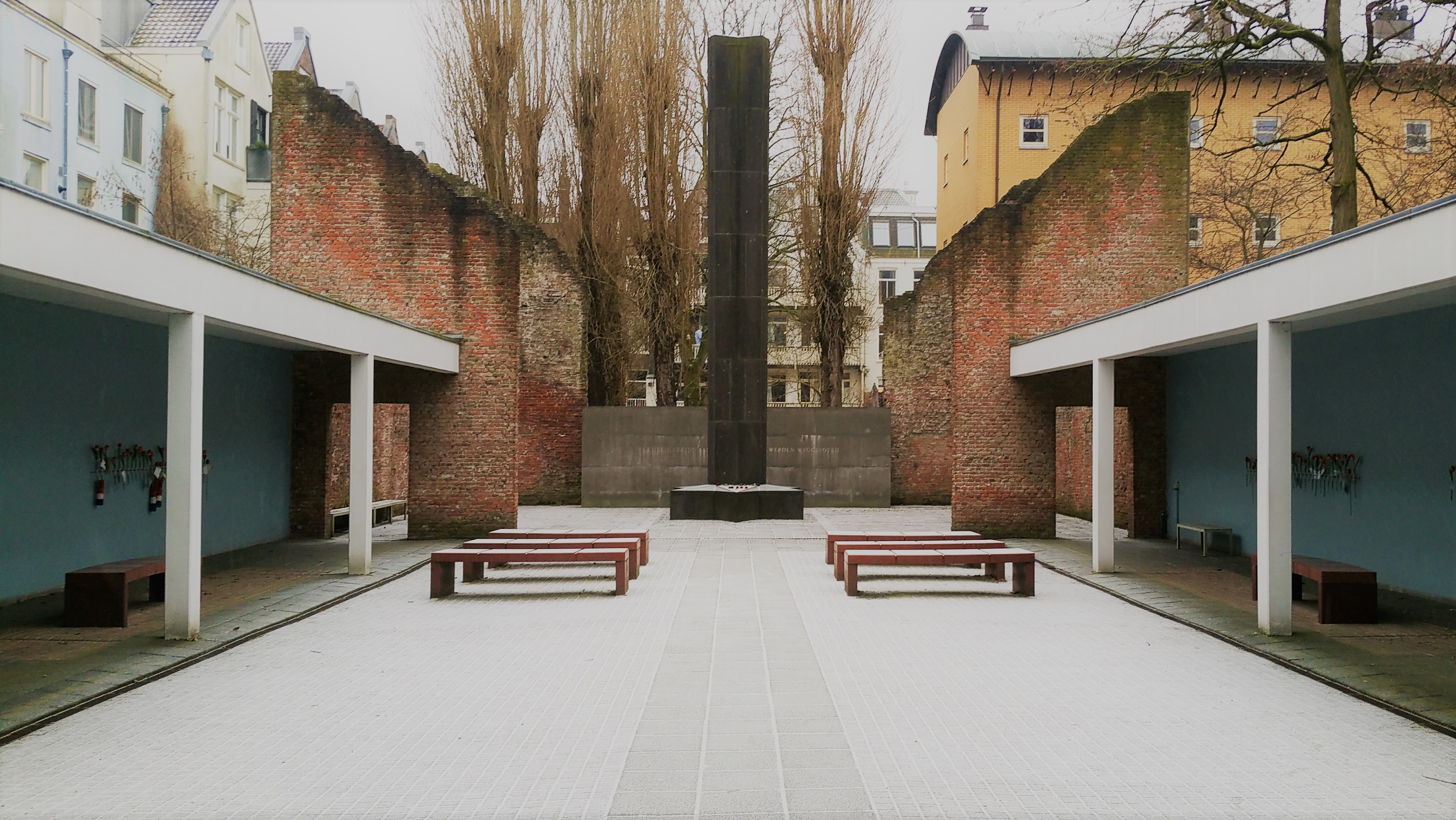 a monument with benches, in between old brick walls and houses
