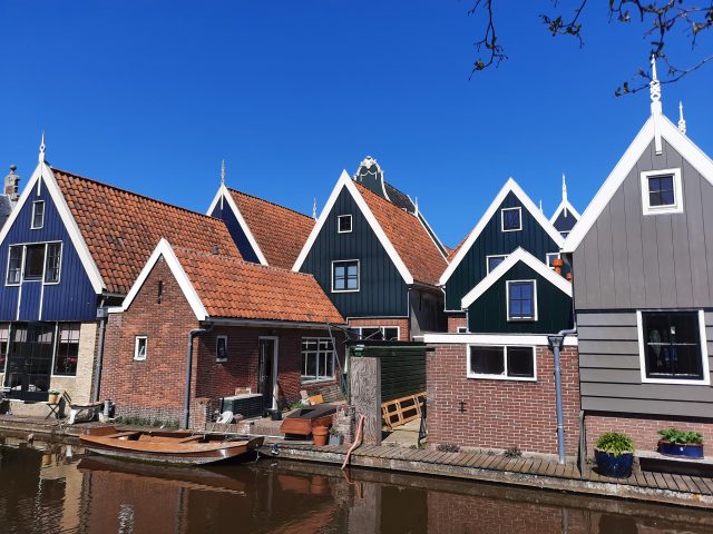 Black wooden houses with orange steep roofs at a canal under a clear sky