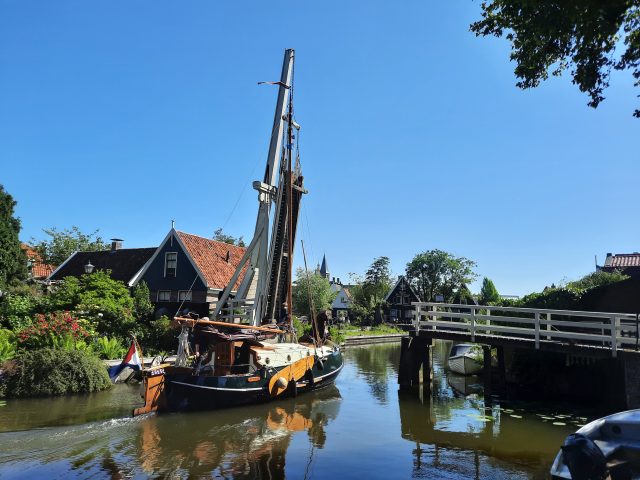 a traditional boat passing a draw bridge under a blue sky