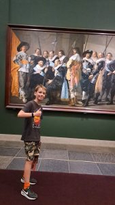 a young boy standing in front of a group painting by Frans Hals