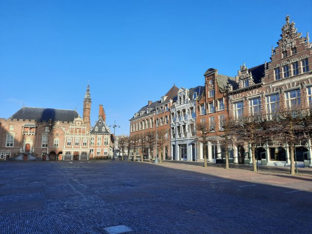 an empty square with trees and old houses on the side under a blue sky