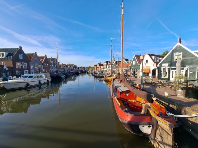 A harbour with calm water and traditional boats in betwee houses under a blue sky