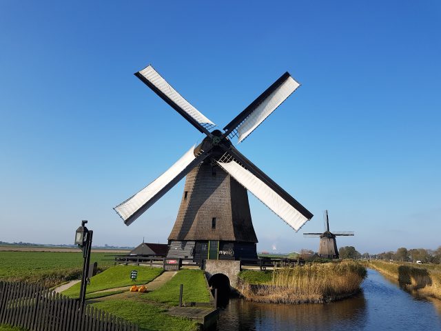 Two windmills near a canal and a green field under a blue sky