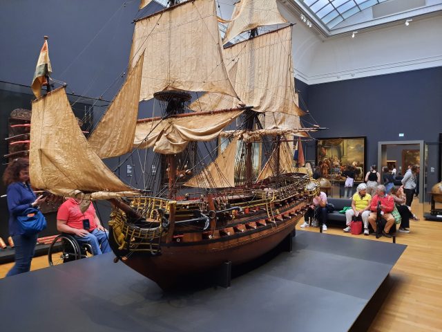 A miniature version of an old ship with sails, with people sitting and standing around it