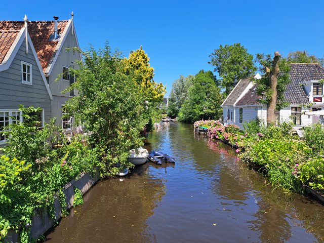 A canal with small boats in between wooden houses under a blue sky
