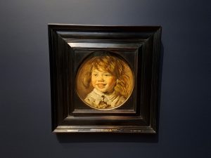 A painting of a laughing boy with wild hair and browning teeth